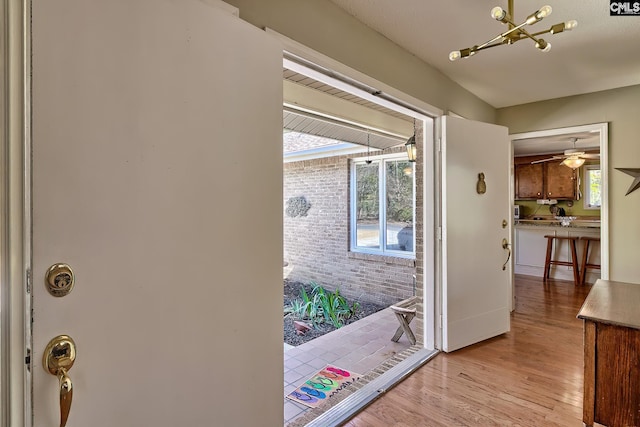 doorway to outside with ceiling fan, brick wall, and light wood-style flooring