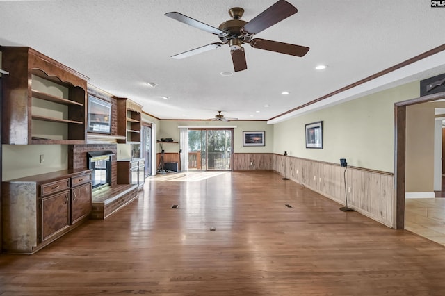 unfurnished living room with a textured ceiling, a fireplace, wood finished floors, and wainscoting