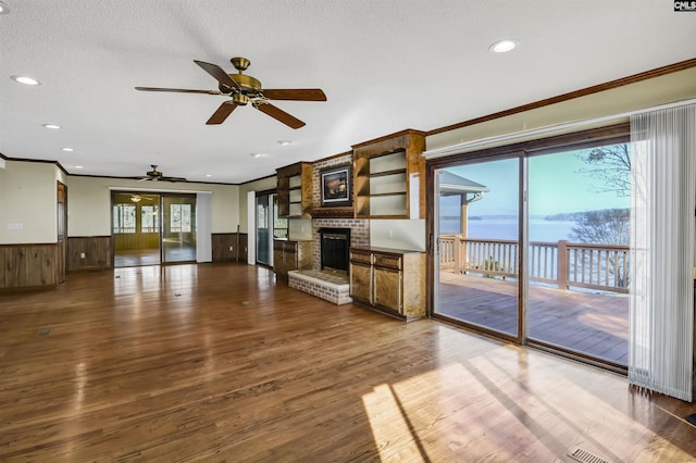 unfurnished living room featuring a wainscoted wall, a fireplace, a wealth of natural light, and wood finished floors