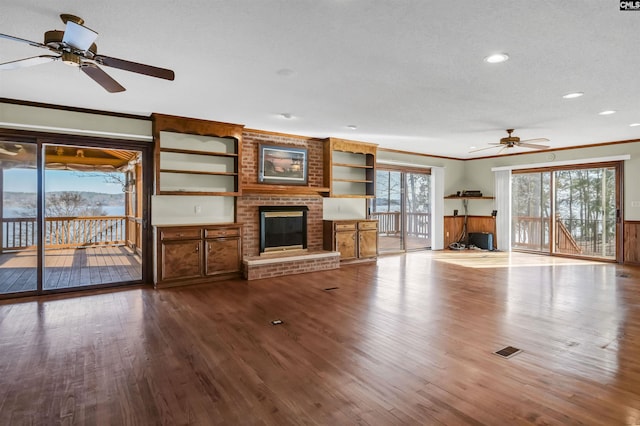 unfurnished living room with crown molding, a fireplace, recessed lighting, a textured ceiling, and wood finished floors