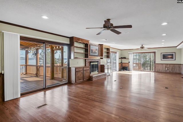 unfurnished living room with crown molding, a fireplace, visible vents, wainscoting, and wood finished floors