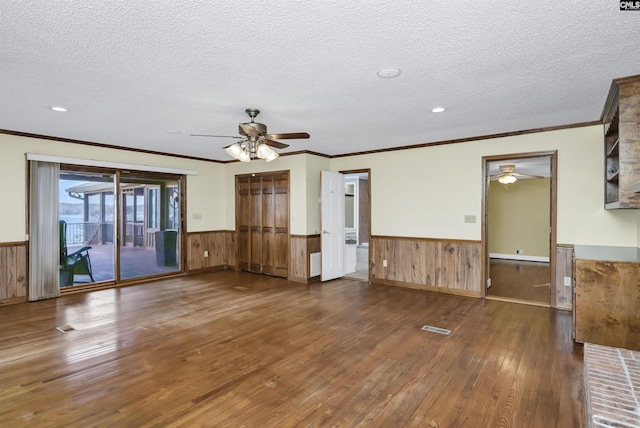 unfurnished living room featuring hardwood / wood-style flooring, a wainscoted wall, visible vents, and a textured ceiling