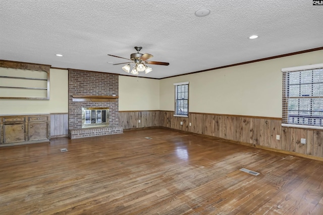 unfurnished living room with a wainscoted wall, visible vents, a brick fireplace, a textured ceiling, and hardwood / wood-style flooring