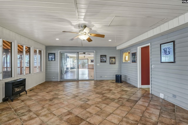 unfurnished sunroom featuring a wood stove and a ceiling fan