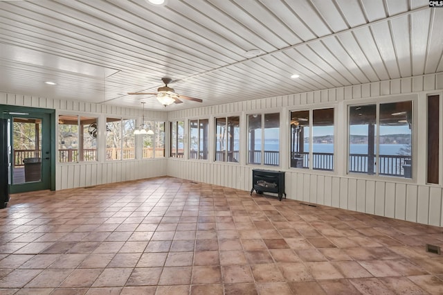 unfurnished sunroom with visible vents, a wood stove, a water view, and a ceiling fan