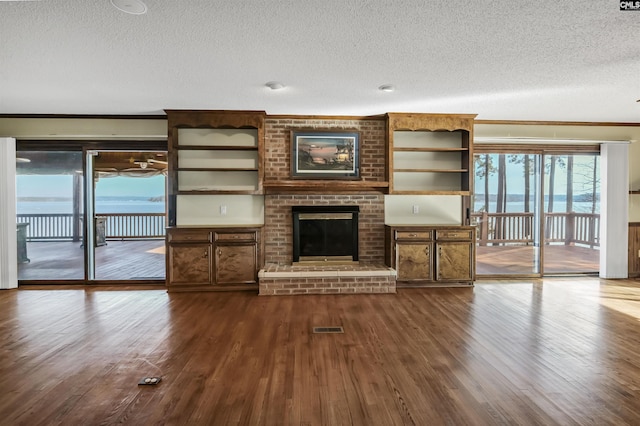 unfurnished living room with dark wood-style floors, a textured ceiling, a brick fireplace, and visible vents