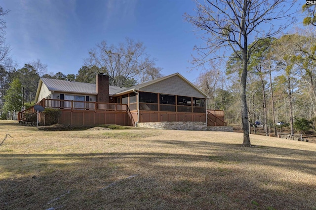 back of house with a chimney, a lawn, a sunroom, metal roof, and a wooden deck