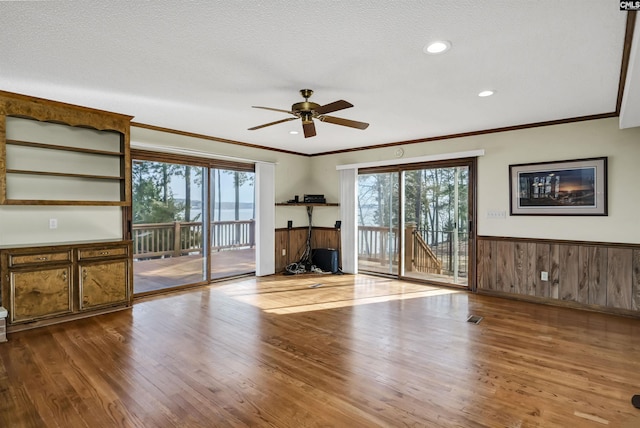 unfurnished living room with a healthy amount of sunlight, a wainscoted wall, crown molding, and wood finished floors