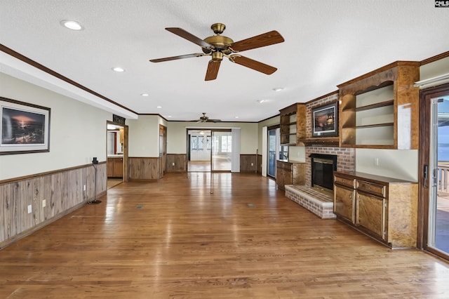 unfurnished living room featuring a textured ceiling, light wood-type flooring, wainscoting, and a fireplace