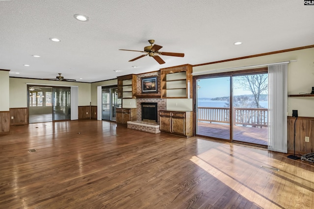 unfurnished living room with dark wood-style flooring, a wainscoted wall, ornamental molding, a brick fireplace, and a textured ceiling