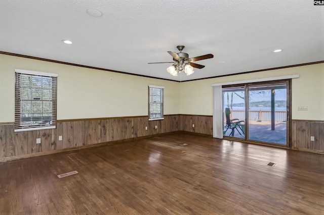 spare room featuring visible vents, a wainscoted wall, wood finished floors, a textured ceiling, and wood walls