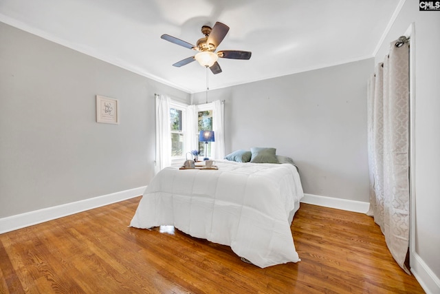 bedroom featuring ceiling fan, baseboards, wood finished floors, and ornamental molding