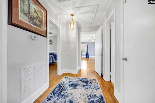 corridor with visible vents, light wood-style flooring, attic access, ornamental molding, and baseboards