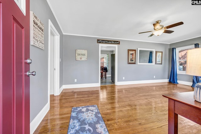 foyer with ornamental molding, a ceiling fan, baseboards, and wood finished floors