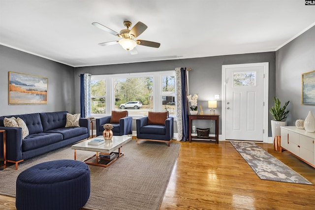 living room featuring a ceiling fan, crown molding, baseboards, and wood finished floors