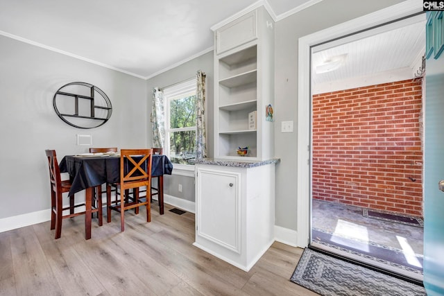 dining room with ornamental molding, brick wall, baseboards, and light wood finished floors