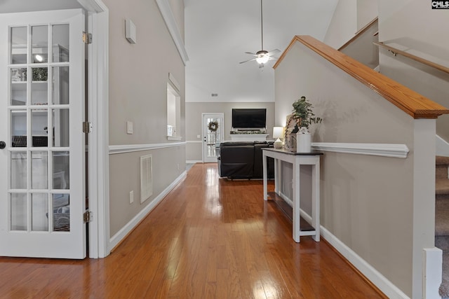 corridor with visible vents, baseboards, wood-type flooring, stairway, and high vaulted ceiling