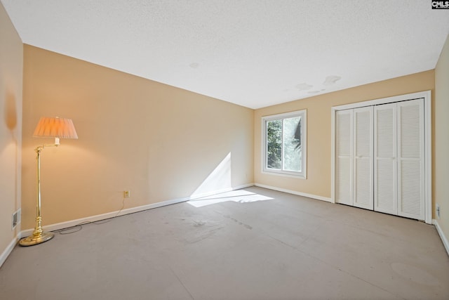 unfurnished bedroom with a textured ceiling, concrete floors, visible vents, baseboards, and a closet