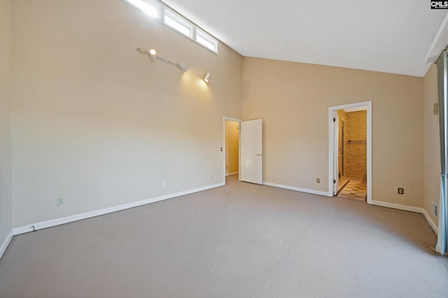 empty room with high vaulted ceiling, concrete floors, and baseboards