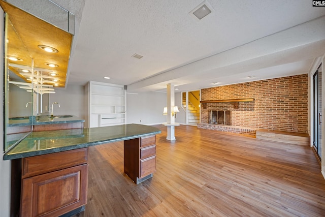 kitchen with a fireplace, a sink, a textured ceiling, brick wall, and light wood-type flooring