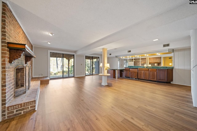 unfurnished living room with a brick fireplace, a textured ceiling, light wood-style floors, and ornate columns