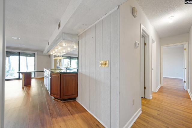 corridor with baseboards, visible vents, light wood-style flooring, and a textured ceiling