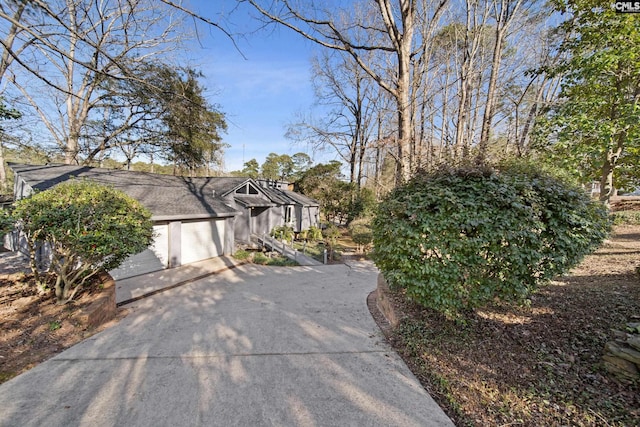 view of side of home featuring concrete driveway, a shingled roof, and an attached garage