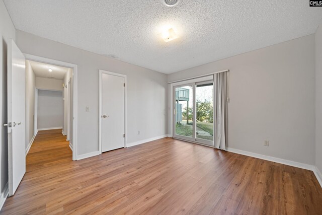 empty room with a textured ceiling, light wood-style flooring, and baseboards