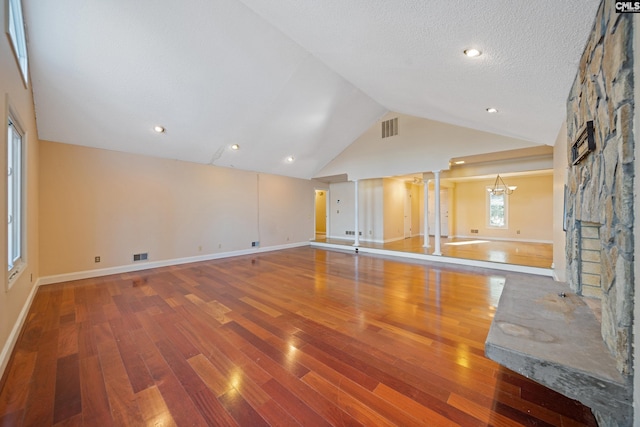 unfurnished living room with lofted ceiling, an inviting chandelier, visible vents, and a stone fireplace