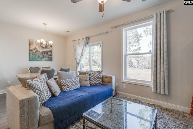 living room with ceiling fan with notable chandelier and baseboards