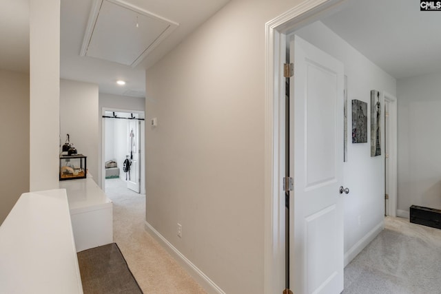 hallway featuring attic access, light carpet, and baseboards