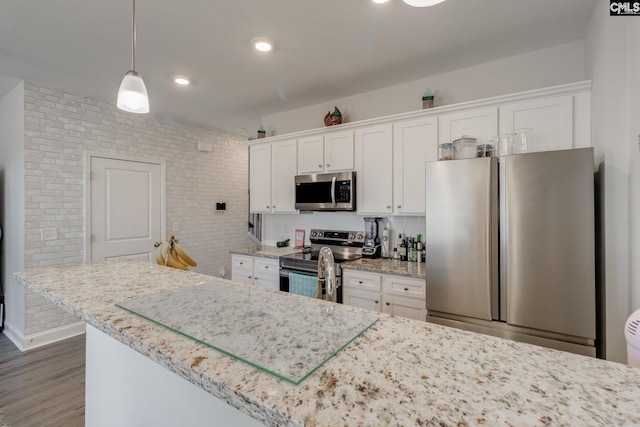 kitchen with decorative backsplash, appliances with stainless steel finishes, wood finished floors, decorative light fixtures, and white cabinetry