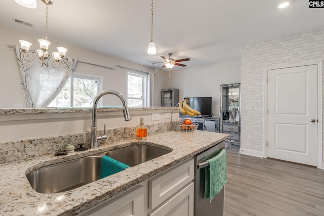 kitchen featuring decorative light fixtures, light wood-style flooring, stainless steel dishwasher, a sink, and light stone countertops