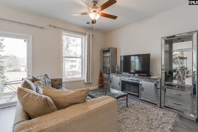 living room with visible vents, wood finished floors, and a ceiling fan