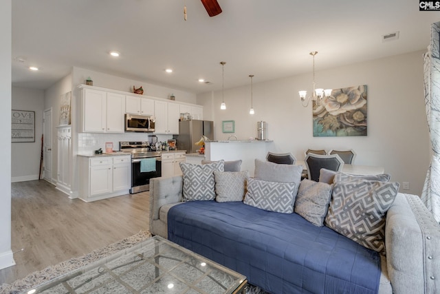 living room with recessed lighting, visible vents, light wood-style floors, baseboards, and ceiling fan with notable chandelier