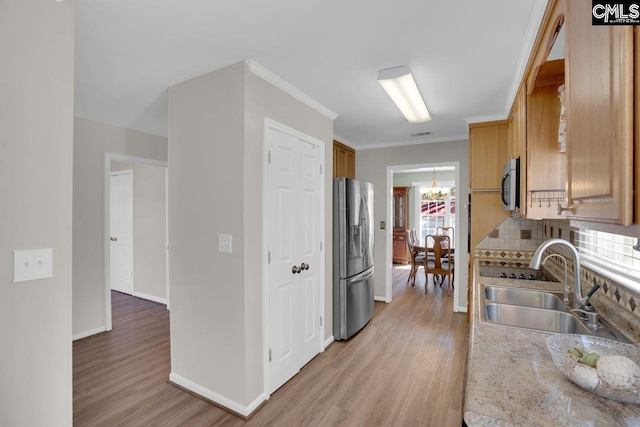 kitchen with tasteful backsplash, light wood-type flooring, ornamental molding, stainless steel appliances, and a sink