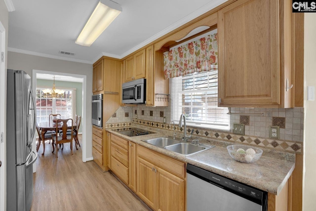 kitchen with a sink, light countertops, light wood-style floors, appliances with stainless steel finishes, and crown molding