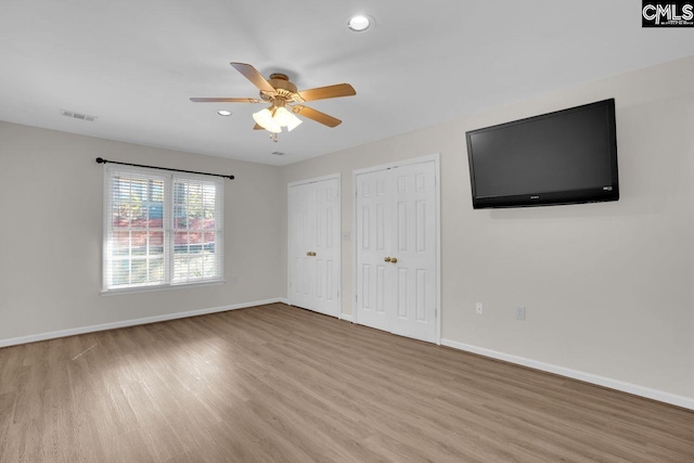unfurnished bedroom featuring baseboards, light wood finished floors, visible vents, ceiling fan, and two closets