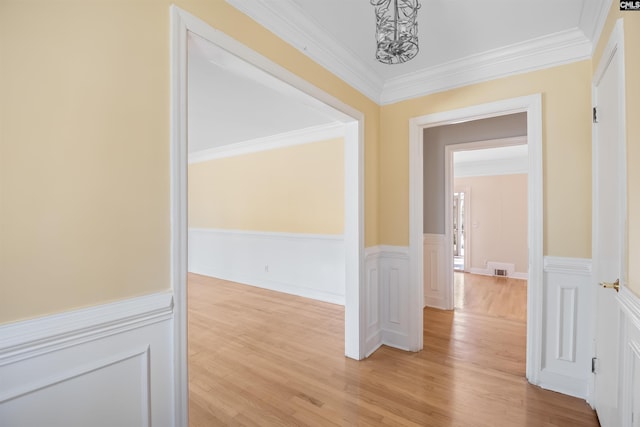 hallway with ornamental molding, light wood finished floors, wainscoting, and a decorative wall