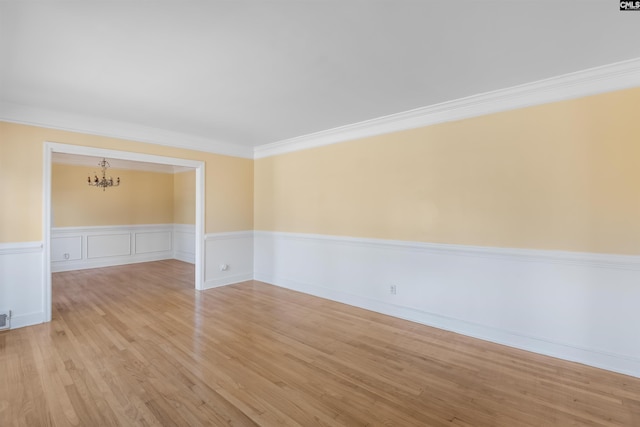 spare room featuring a wainscoted wall, light wood-style flooring, ornamental molding, and a chandelier