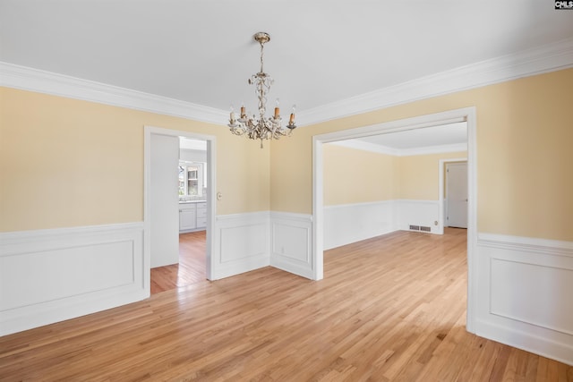 unfurnished dining area featuring crown molding, visible vents, light wood-style floors, wainscoting, and a chandelier