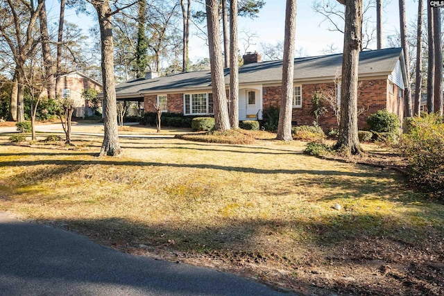 ranch-style home with brick siding, a chimney, a carport, driveway, and a front lawn