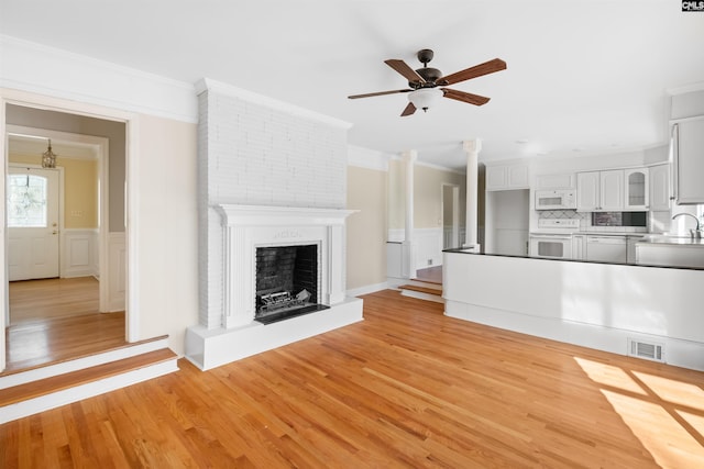 unfurnished living room with crown molding, a fireplace, visible vents, ceiling fan, and light wood-type flooring