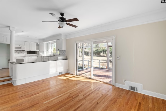 unfurnished living room with baseboards, visible vents, light wood-style flooring, ceiling fan, and a sink