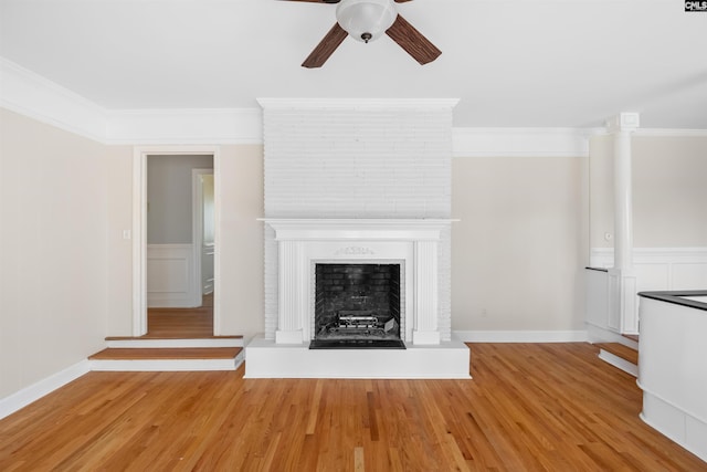 unfurnished living room featuring ornamental molding, a fireplace with raised hearth, ceiling fan, and wood finished floors