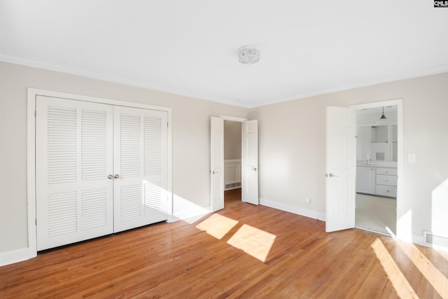 unfurnished bedroom with visible vents, baseboards, ornamental molding, light wood-style floors, and a closet