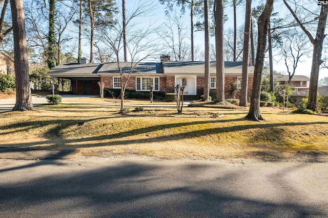 view of front of property featuring driveway, brick siding, a chimney, and an attached carport