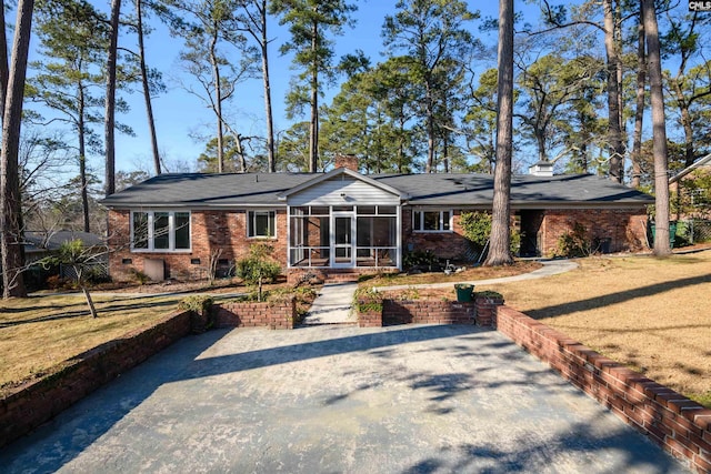 ranch-style home with aphalt driveway, brick siding, a sunroom, a front lawn, and a chimney