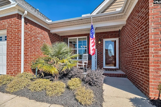 view of exterior entry featuring brick siding, a porch, and an attached garage