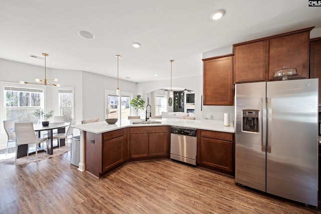 kitchen with a peninsula, dark wood-style flooring, a sink, light countertops, and appliances with stainless steel finishes